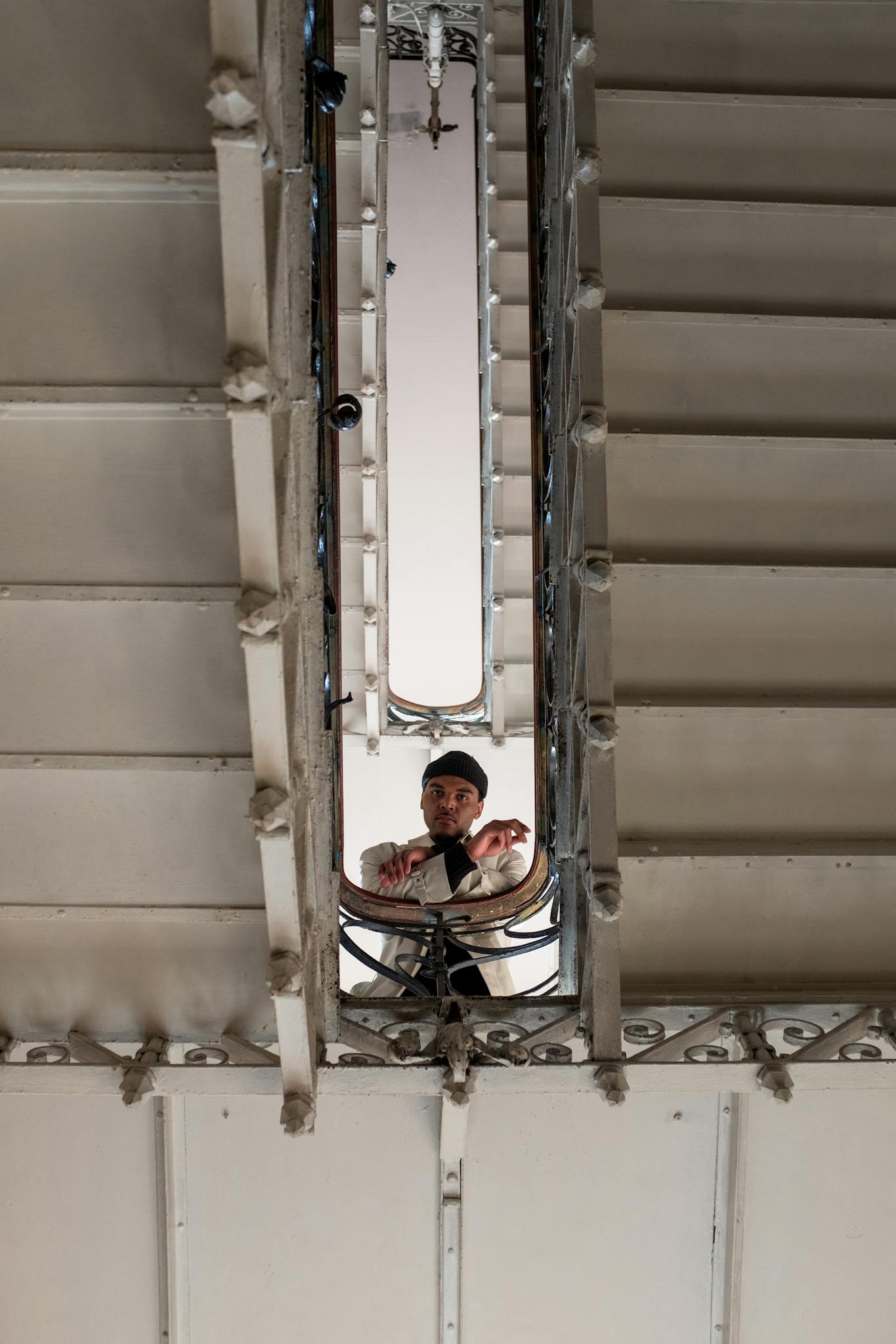 A man at the bottom of a vintage spiral staircase, seen through the opening.